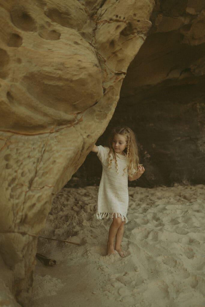 Little girl playing in the caves at Chinamens Beach at Evans Head NSW wearing a crochet dress from The Sunday Shop