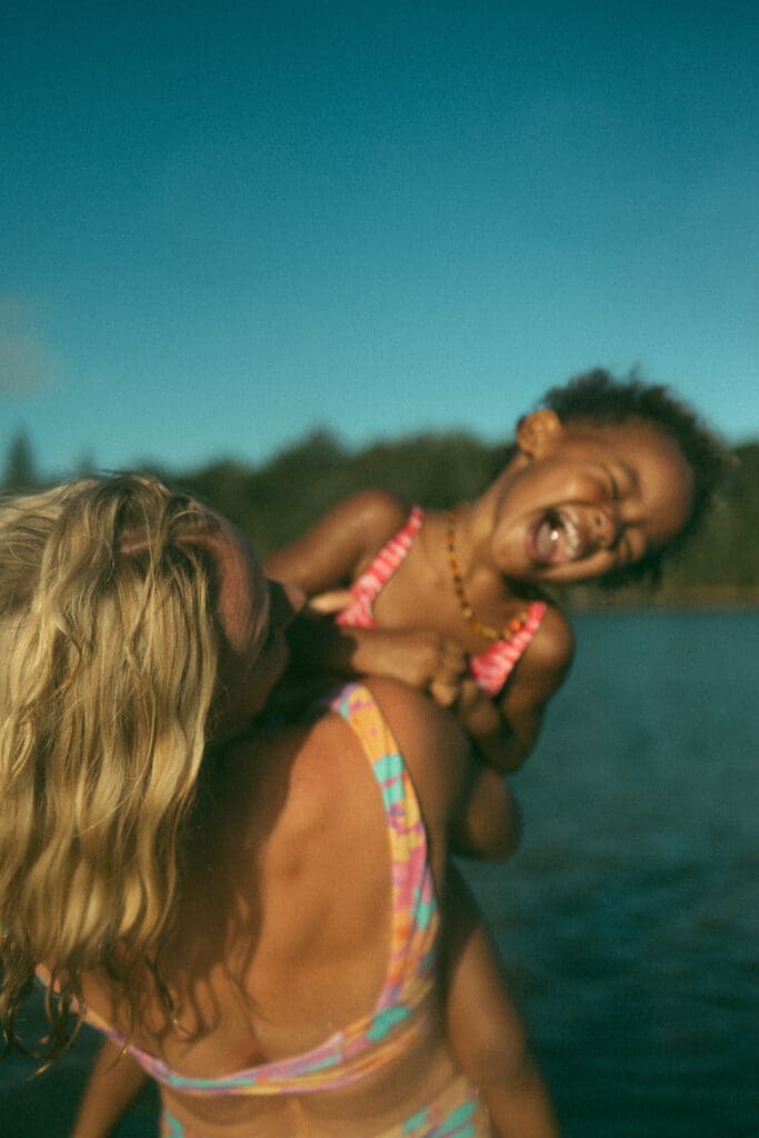 Little girl laughing as her mum tickles her on the shoreline of Evans River in Evans Head NSW